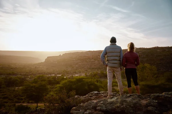 Vista trasera del joven hombre y la mujer de pie en el acantilado de la montaña mirando al amanecer — Foto de Stock