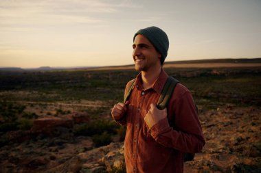 Sırt çantalı gülen yürüyüşçü, güneşin doğuşunu seyrediyor.