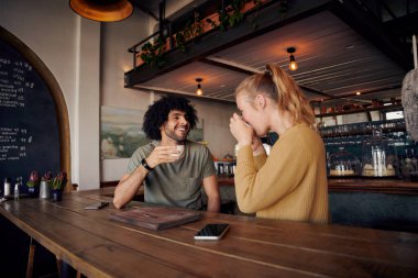 Yakışıklı genç adam modern kafede kahve içen bir kadınla konuşuyor.