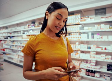 Eczanede rafta duran akıllı telefonu kullanan genç bir kadın.