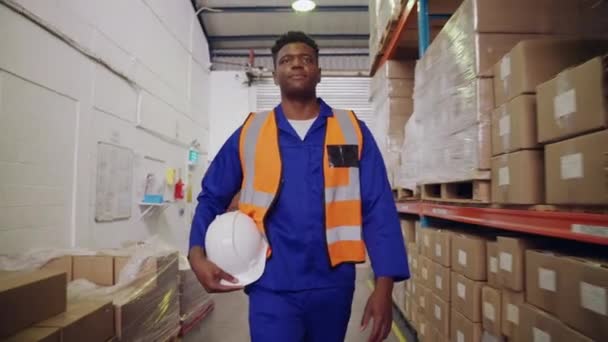 Kendine güvenen Afrikalı bir depo çalışanının büyük bir dağıtım deposunda elinde kasketle yürürken görüntüsü. — Stok video