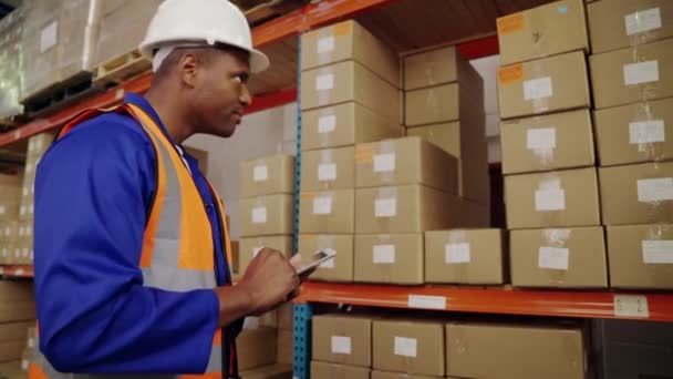 Almacén africano trabajador masculino usando hardhat usando tableta en un almacén grande — Vídeos de Stock