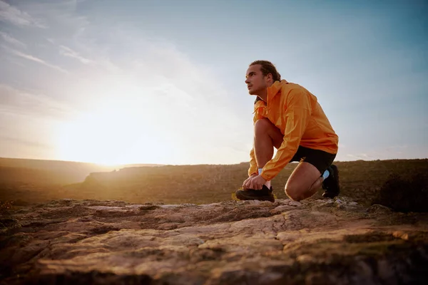 Ajuste jogger masculino atando cordones de zapatos preparándose para el sendero de montaña a través del país en la naturaleza y mirando hacia otro lado contra el amanecer —  Fotos de Stock