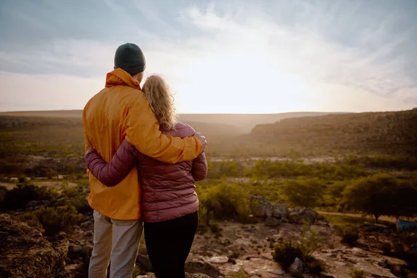 Vista trasera de la joven pareja enamorada abrazando mientras mira el hermoso amanecer después de caminar hasta el borde del acantilado de la montaña — Foto de Stock