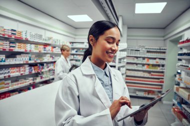 Tıbbi mağazada dijital tablet kullanan gülümseyen genç bir kadın.