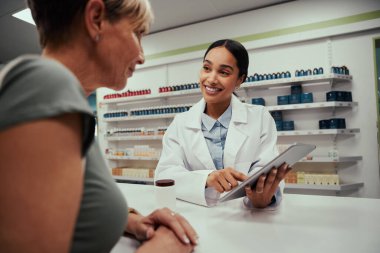 İlaç kullanırken ekranı dijital tablette tutarken ve gösterirken müşteriyle konuşan mutlu eczacı