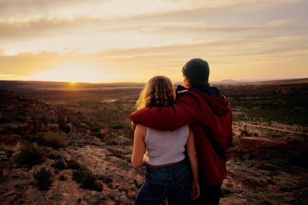 Vista trasera de la joven pareja disfrutando juntos viendo hermoso amanecer de pie en la montaña — Foto de Stock