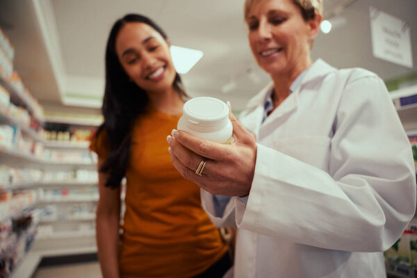 Закрытие рук старшей аптекарши, помогающей клиентке найти бутылку с лекарствами с полок