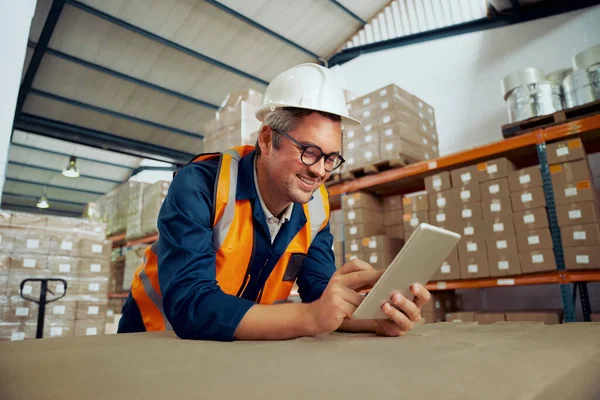 Felice dipendente industriale maschio controllo tablet digitale indossando abbigliamento da lavoro protettivo a magazzino — Foto Stock