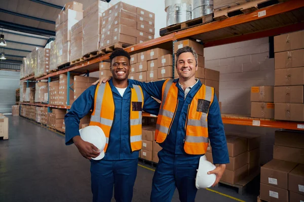 Retrato sorridente de dois trabalhadores de armazém multi étnico segurando chapéu de segurança na mão na fábrica — Fotografia de Stock