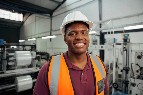 Retrato sorridente de um jovem trabalhador da fábrica usando capacete no armazém — Fotografia de Stock