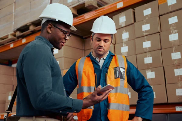 Engenheiros de fábrica multirracial olhando para tablet digital com caixas empilhadas em segundo plano — Fotografia de Stock