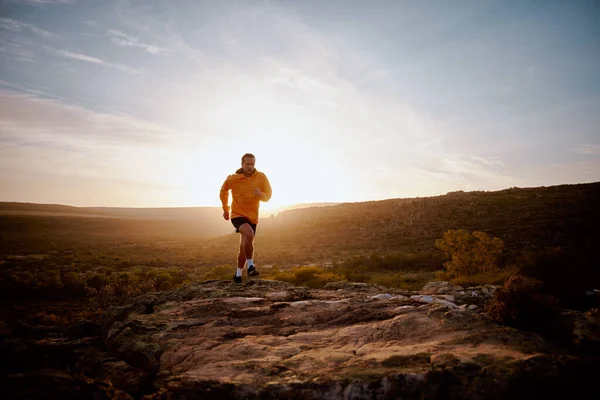 Joven atleta masculino en forma corriendo sobre un sendero rocoso de montaña en la colina durante el amanecer —  Fotos de Stock