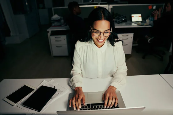 Jovem empresária positiva usando laptop em sua mesa com colegas de fundo no escritório — Fotografia de Stock