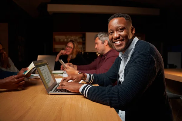Porträtt av leende ung afrikansk affärsman med hjälp av sin bärbara dator tittar på kameran samtidigt ha möte med sin kollega — Stockfoto