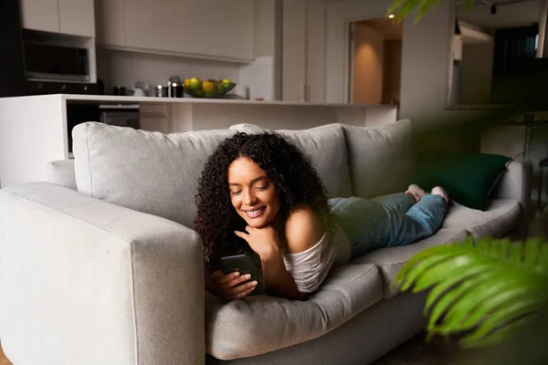 Gemengde race vrouwelijke ontspannen op bank sms vriendje glimlachen — Stockfoto