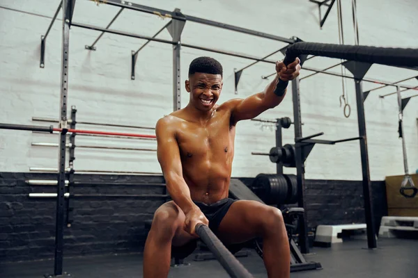 Jovem afro-americano se exercitando dentro de um ginásio. Topless personal trainer masculino usando corda para fortalecer seus braços. Foto de alta qualidade — Fotografia de Stock