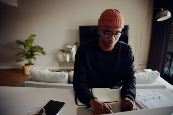 Homme afro-américain travaillant à la maison et naviguant sur son ordinateur portable. Un Afro-Américain écrivant des notes et tapant sur son ordinateur portable. Photo de haute qualité — Photo