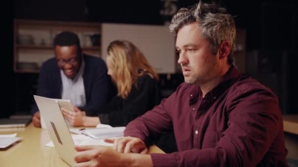 Diverso grupo de colegas trabalhando até tarde da noite no escritório discutindo ideias para novo projeto sentado em torno da mesa rindo — Vídeo de Stock