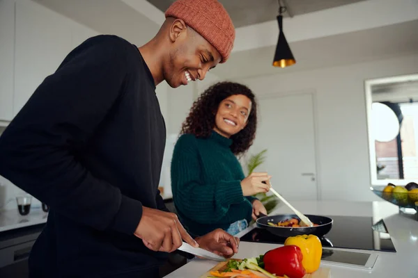 Young mixed race couple cooking food in the kitchen at home. Happy couple preparing food and smiling. High quality photo — Stock Photo, Image