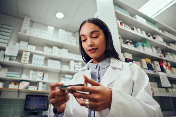 Low angle view of woman pharmacist wearing labcoat uniform reading medicine name in chemist