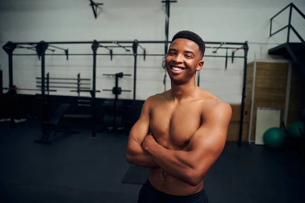 Afroameričan stojí se zkříženýma rukama a usmívá se do kamery. Muž sportovec vypadá šťastně při cvičení v tělocvičně. Kvalitní fotografie — Stock fotografie