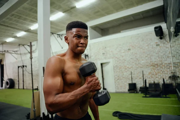 Afroamerikaner halten Gewichte während eines intensiven Trainings. Der männliche Athlet betrachtet sich selbst im Turnspiegel, während er Hanteln hebt. Hochwertiges Foto — Stockfoto