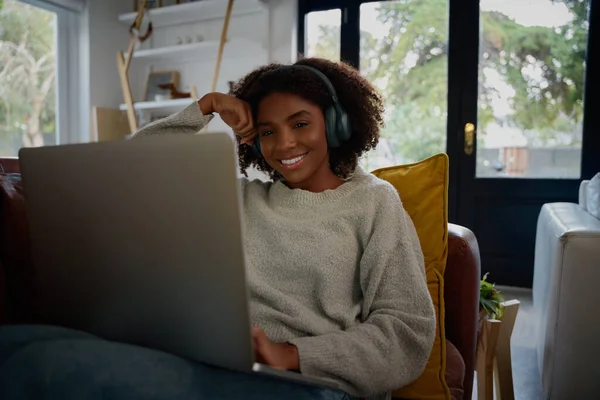 Fröhliche Afrikanerin hört Audio über Kopfhörer, während sie zu Hause Videos auf dem Laptop anschaut — Stockfoto