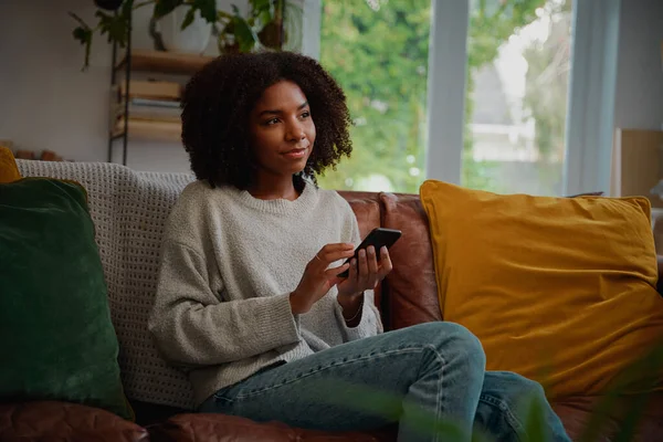 Vrouw denken terwijl het houden van smartphone in de hand voor het typen van bericht — Stockfoto