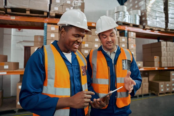 Trabalhadores industriais felizes em chapéu branco e colete de proteção olhando para tablet digital — Fotografia de Stock