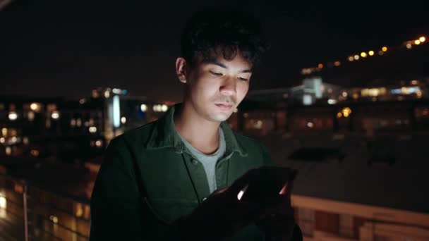 Mixte jeune homme debout sur le balcon bavarder avec des amis sur l'appareil cellulaire défilant sur les médias sociaux — Video