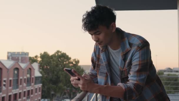 Gemengde race mannelijke sms 'en op cellulaire apparaat messaging vrienden terwijl leunend over balkon — Stockvideo