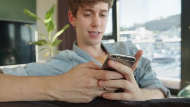 ソファの上でリラックスした携帯電話上の白人男性テキストメッセージ友人とのアレンジ — ストック動画