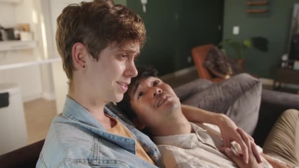 युवा जोड़े मिश्रित दौड़ समलैंगिक जोड़ी टेलीविजन देखते हुए जबकि मुस्कुराते हुए एक दूसरे पर — स्टॉक वीडियो