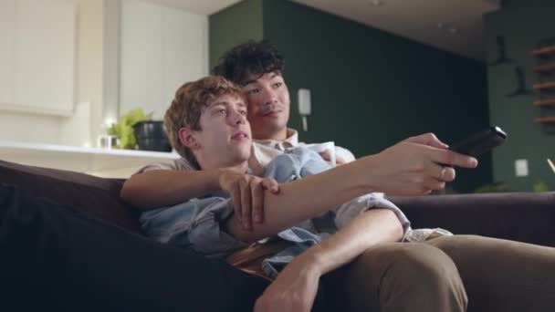 Młody mężczyzna gej para oglądanie TV razem na kanapa siedzi w domu podczas izolacja — Wideo stockowe