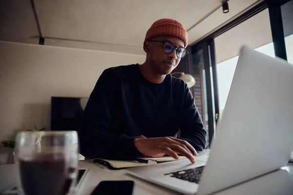 En afroamerikansk man som jobbar hemifrån och surfar på sin laptop. Afroamerikansk man som använder elektronik för att arbeta hemifrån. Högkvalitativt foto — Stockfoto