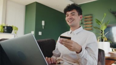 Karışık ırktan gülümseyen bir erkek kredi kartı tutarken ve dizüstü bilgisayar kullanırken online ürün satın alıyor.