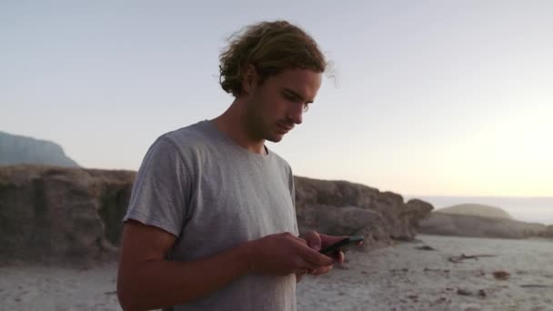 En ung, hvit mann som tekstet på telefonen under solnedgang. Nære på at mannen ser på telefonen. Opptak av høy kvalitet på 4k – stockvideo