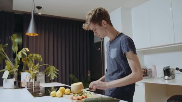 Кавказький самець рубає овочі на кухні, готуючи здорову їжу для партнера. — стокове відео