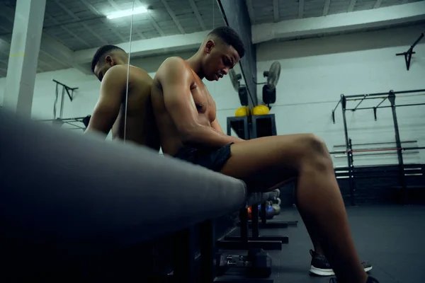 Jovem atleta afro-americano descansando no ginásio depois de um duro treinamento cruzado. Sem camisa mestiço mestiço macho sentado após o exercício. Foto de alta qualidade — Fotografia de Stock