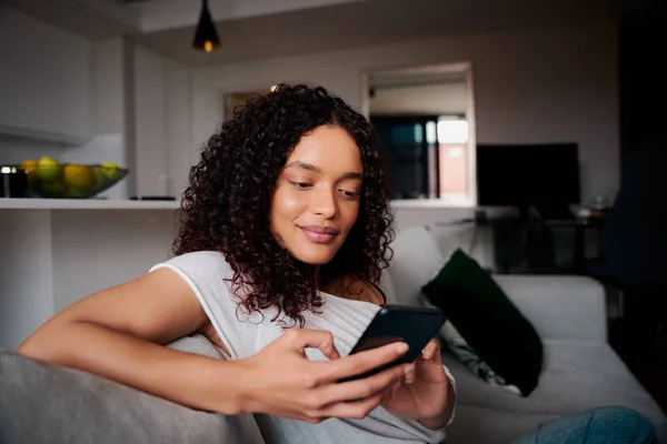 Mixte race afro-américaine femme relaxant sur canapé textos sur appareil cellulaire — Photo