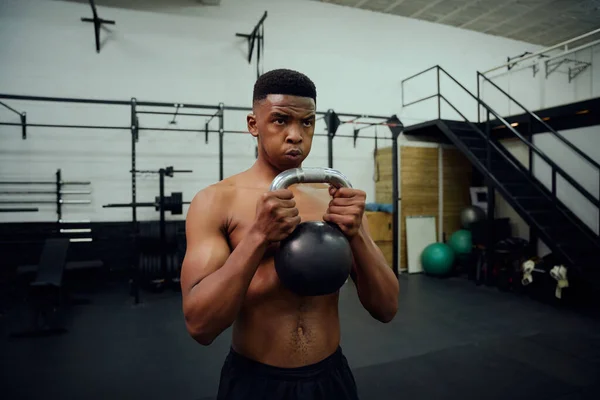 Afroamerikaner beim Crosstraining im Fitnessstudio. Mischlingsrüde mit einer Kettlebell während des Trainings. Hochwertiges Foto — Stockfoto