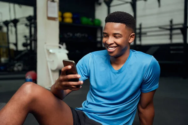Hombre afroamericano mirando su teléfono. Primer plano de las aplicaciones de desplazamiento masculino en su teléfono mientras descansa en el gimnasio. Foto de alta calidad —  Fotos de Stock