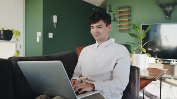 Gemengde race mannelijke werken op laptop ontspannen op de bank in huis werken aan business project — Stockvideo