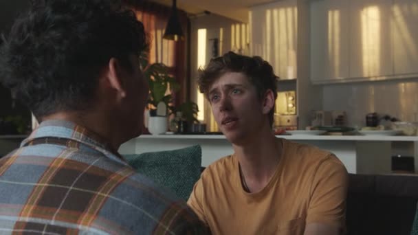 Мужская пара смешанной расы вступает в интенсивный разговор, проявляя привязанность в гостиной — стоковое видео