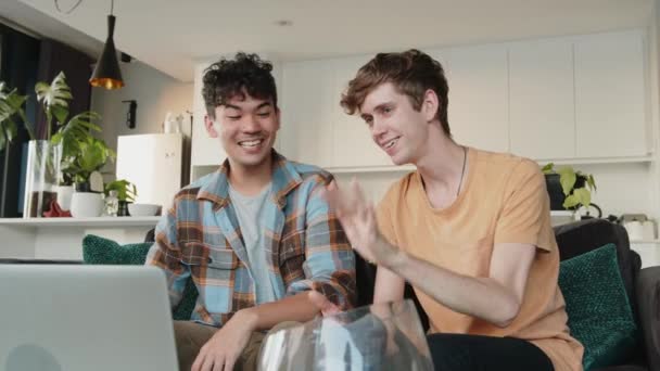 Jovem casal caucasiano do sexo masculino envolvidos em chamada de vídeo com a família acenando para a tela do computador — Vídeo de Stock