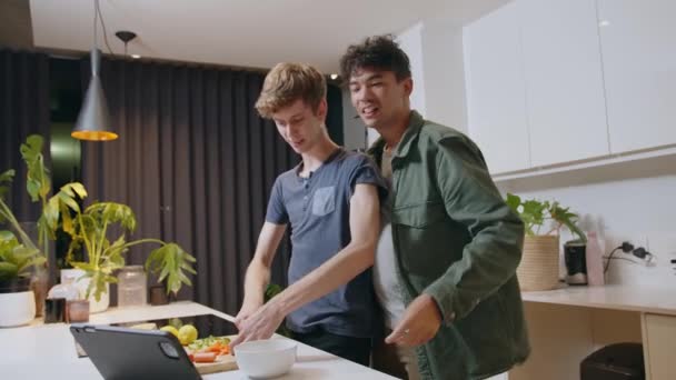 Happy male couple showing affection in kitchen searching recipe on digital tablet — Stock Video