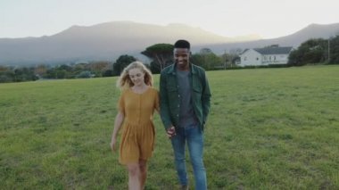 Karışık ırk çiftleri yeşil çimlerde romantik bir şekilde yürüyor 