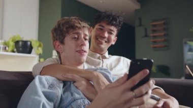 Karışık ırk erkek çifti kanepeye oturup öpüşürken cep telefonu cihazını tutuyor ve dinleniyor.