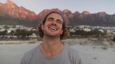 Gün batımında kumsalda gülen kıvırcık saçlı beyaz bir erkek. Yüksek kalite 4k görüntü 